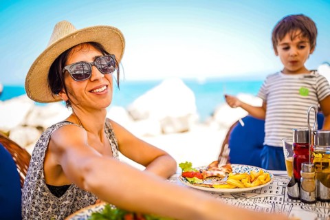 Mother and son enjoying a relaxed meal with grilled fish and fries at a seaside restaurant during