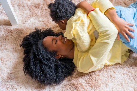 Top view of an african happy mother embracing her little girl lying on the floor