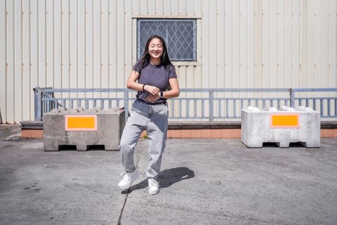 Frontal full length photo of a smiling young asian woman dancing K-pop in an industrial roof