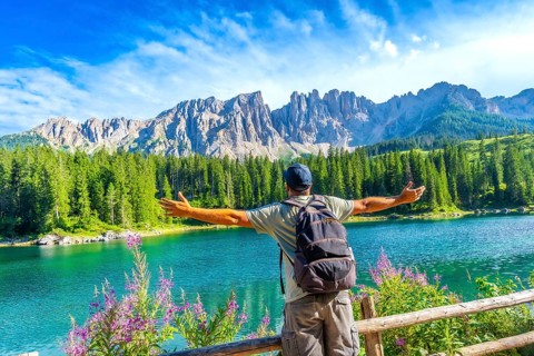 Hiker embracing the stunning panorama of lake carezza with the latemar mountain range in the