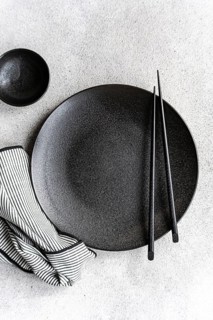A minimalist black and white table setting featuring a textured dark plate, matching bowl, pair of