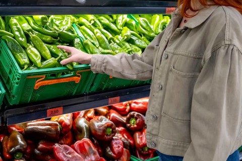 Woman's hand selecting fresh green peppers from a vibrant display in the produce section of a
