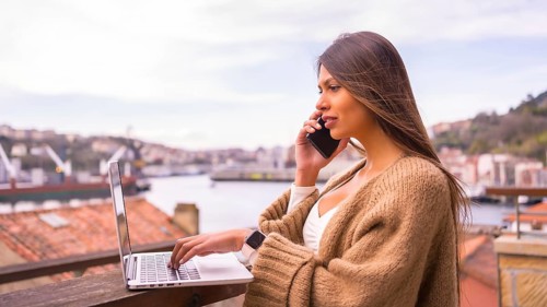 A young Latin woman with a white t-shirt and a brown wool sweater, teleworking on the terrace of a
