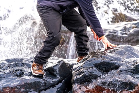 A man is standing on a rock with his hand on a wet rock. The man is wearing a black jacket and