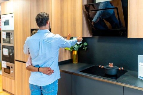 Young couple exploring kitchen design options and appliances, looking at wooden cabinets and modern