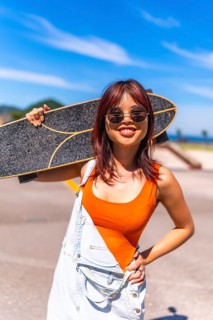 Vertical portrait of a young woman in summer clothes and sunglasses carrying skate on shoulders