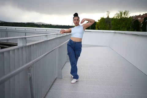 A woman in blue jeans and a blue tank top is posing on a railing. The image has a moody, somewhat
