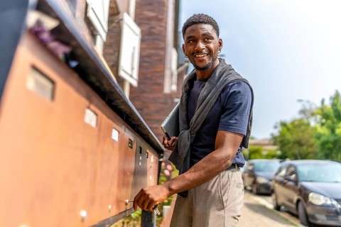 Side view three quarter length photo of a happy and confident african young man checking mailbox in