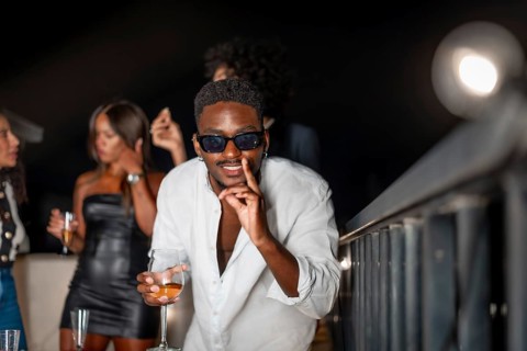 Latin cool man gesturing while dancing and drinking alcohol during roof party at night