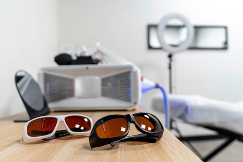 Protective glasses for patient and specialist placed on a wooden table, in an aesthetic medicine