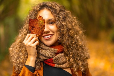 Portrait of a beautiful young woman hiding among yellow leaf outdoors