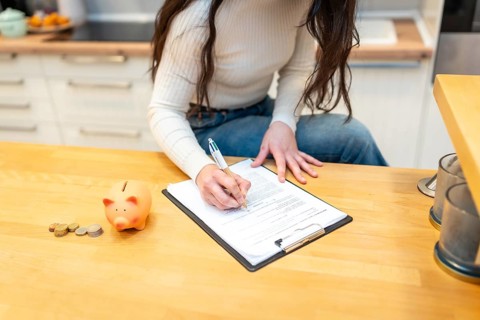 Woman reading and signing an important financial document on a clipboard while managing personal