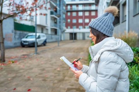 Side view of a caucasian young woman in warm clothes writing notes sitting on the street