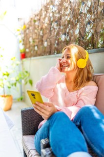 Vertical photo of a caucasian adult woman listening to music and using mobile phone in the