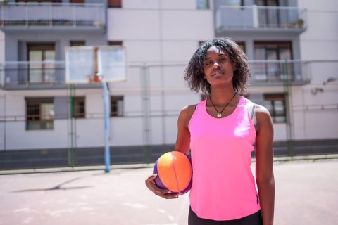 Portrait of a sportive african american female basketball player standing on an urban outdoor court