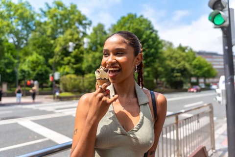 Young woman happily eating an ice cream cone on an urban street during a sunny summer day, enjoying