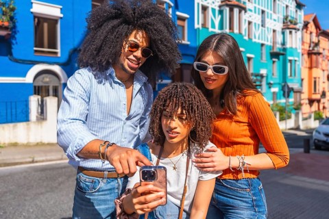 Three young tourists using a smartphone in a colorful street, sharing social media content and