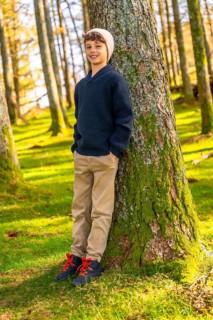 Vertical full length portrait of a caucasian happy boy with casual clothes leaning relaxed on tree
