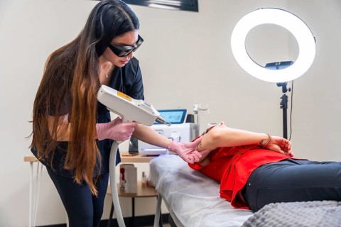 Dermatologist wearing protective eyewear and gloves applying a laser device on a patient's arm to