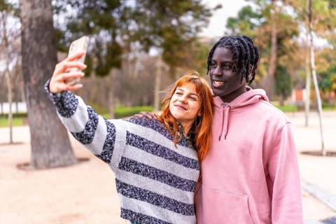 Young interracial couple taking a selfie with a smartphone in a park, enjoying a beautiful day