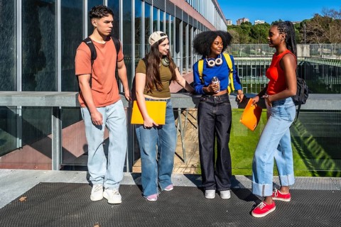 Group of diverse university students standing and talking together on a modern campus walkway with