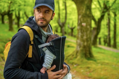 A young father with a yellow backpack and a black cap walking with the newborn child in the