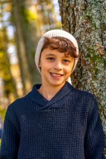Vertical close-up portrait of a urban Teenager with hat leaning in a tree trunk smiling at camera