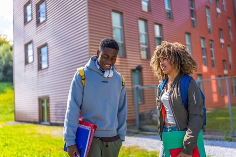 Two male and female multiethnic students reunited backing to university standing chatting outdoors