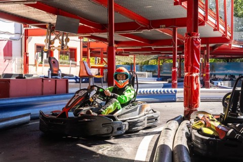 Young driver wearing a bright green suit and an orange helmet, sitting in a go kart on the track,