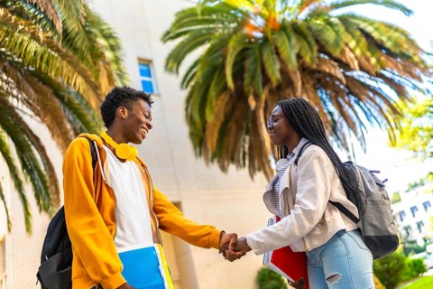 Side view of two young cool african university students shaking hands outside the university