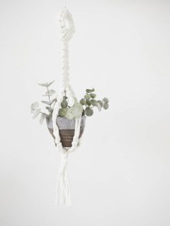 Macrame plant hanger with small branches of dried eucalyptus leaves in gray and brown ceramic pot.