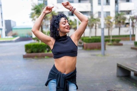 Curly haired woman dancing latin music in the urban park, enjoying freedom and healthy lifestyle