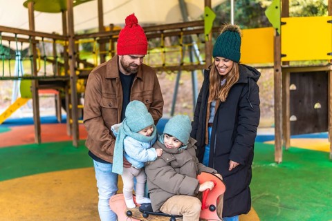 Smiling parents watching their children playing on a rocking horse at the playground during a cold