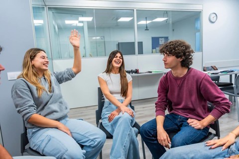 Young university students in a modern classroom laugh, raise hands and share ideas during an