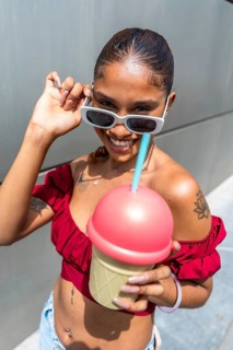 Diverse young woman smiling and holding a novelty ice cream cup with a straw while posing outdoors