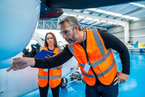 Aviation engineers are meticulously inspecting an airplane engine and structure inside a large