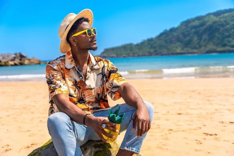 Young man enjoying a refreshing drink while wearing sunglasses and a straw hat, soaking up the sun