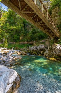 Tourists crossing a wooden footbridge over a clear turquoise river in tolmin gorge, slovenia,
