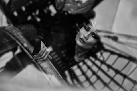 A dramatic black-and-white portrait of a thoughtful woman seen through abstract reflections. The