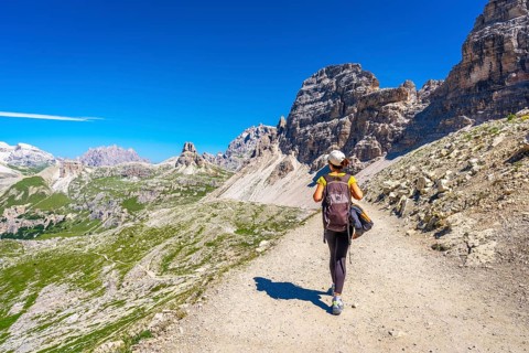 Female hiker walking on a trail in the dolomites mountains with tre cime di lavaredo in the