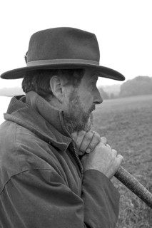 Portrait of a farmer wearing a hat, leaning on a stick while herding his cattle, black and white,