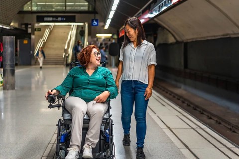 Frontal view of a happy caucasian disabled woman and multi-ethnic friend walking along metro