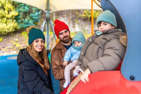Smiling family enjoying a day at the playground, with children playing on a slide during the fall