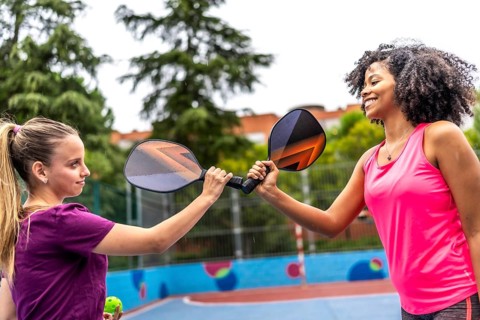 Team of two multi-ethnic women clashing rackets before playing pickelball in an outdoor court