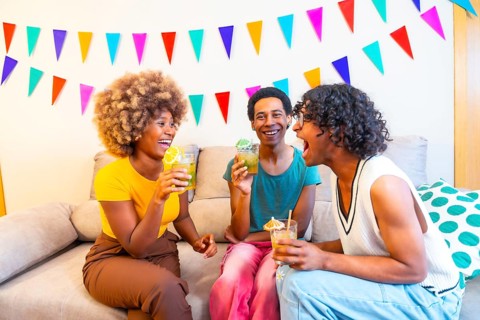 Multi-ethnic friends drinking cocktails on the sofa at a party decorated home