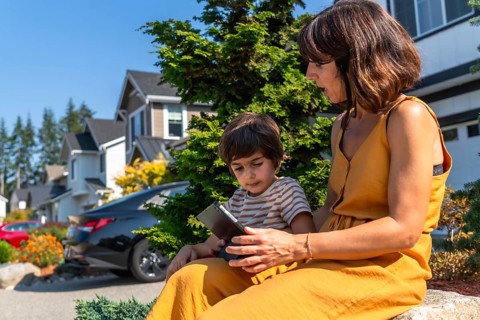 Mother and young son sitting outdoors on a sunny day in a modern suburban neighborhood. Actively