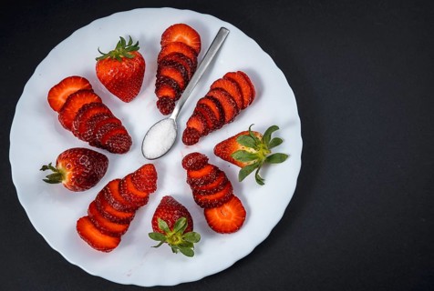 Natural strawberries on a white plate with a spoon of sugar with black background