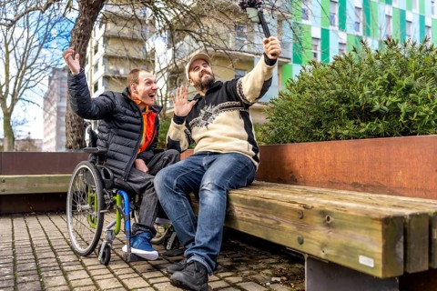 Two cheerful content creators, one in a wheelchair, are recording a video blog using a gimbal in a