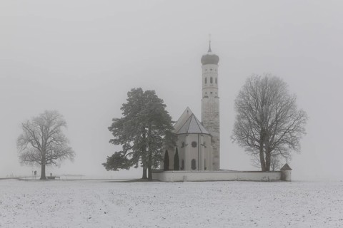 A Gothic church with towers and trees in winter fog, pilgrimage church St. Coloman, near Füssen,