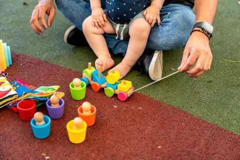 Father and baby boy sitting on rubber playground flooring, engaging in educational play, arranging